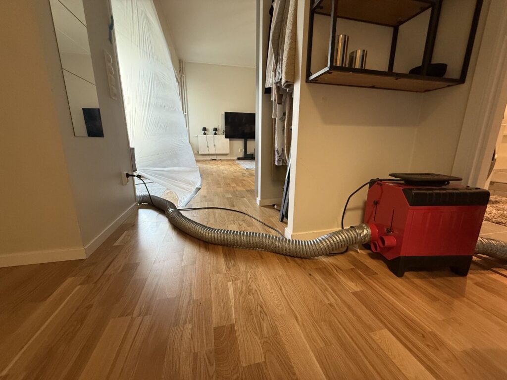 Översiktsbild av avfuktningsinstallation. Skadeområdet har avskärmats med dammskyddsplast och avfuktare har installerats för att påskynda uttorkning av den fuktpåverkade golvkonstruktionen.